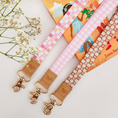 Load image into Gallery viewer, Three colourful fabric wristlet keychains with gold hardware and tan leather ends, featuring pink gingham daisy, blush polka dot stripe, and retro orange checker floral patterns, laid on pastel notebooks with floral accents – Lilly Jayne Collective.