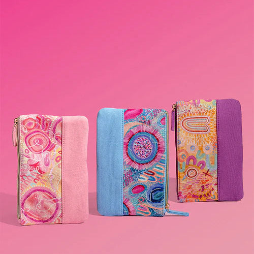 Three colorful zip-around pouches with patterned fabric and solid fabric panels, arranged side by side on a solid pink background.