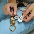 Load image into Gallery viewer, Hands holding a polka dot keychain with a gold ring and a small pouch on a denim surface.