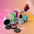 Load image into Gallery viewer, Ink refill kit with ink pads and a hand pouring ink, on a gradient pink and yellow background.
