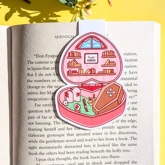 Heart-shaped pink jewelry box with a miniature book and sword on an open book with a yellow background