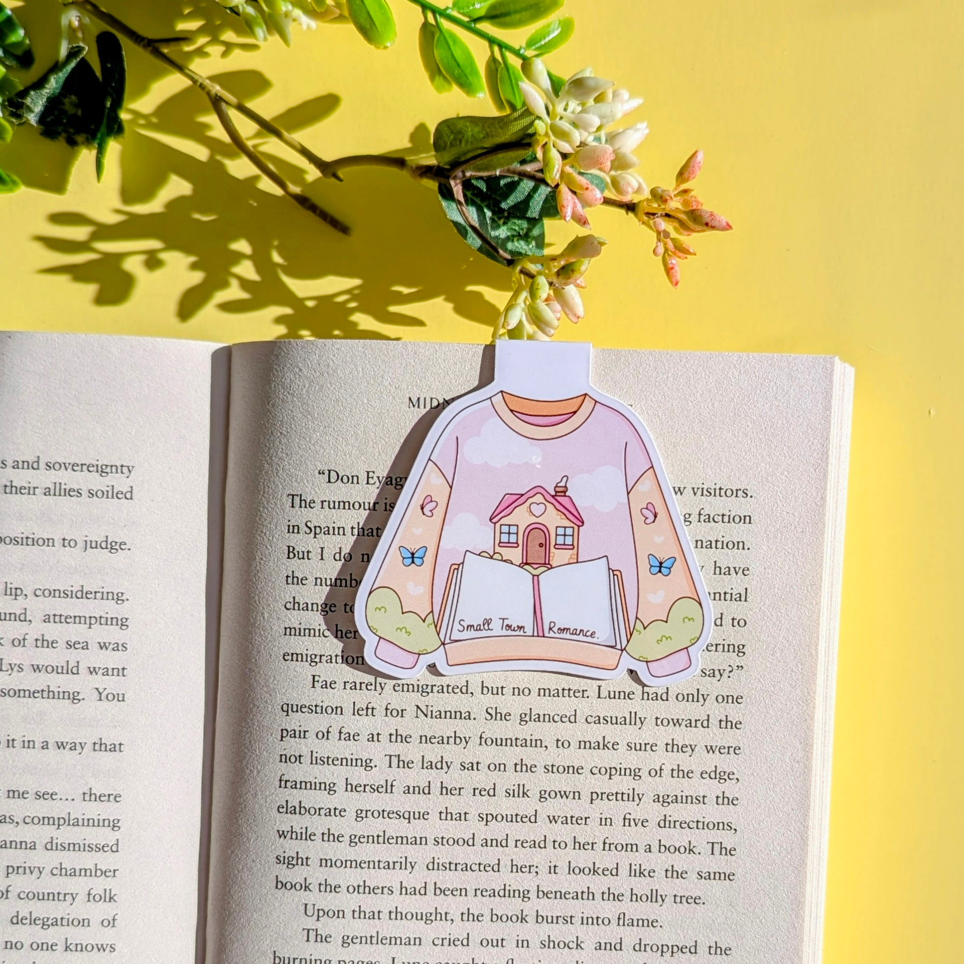 Sticker of a person wearing a sweater with a house design on an open book with a yellow background and flowers.
