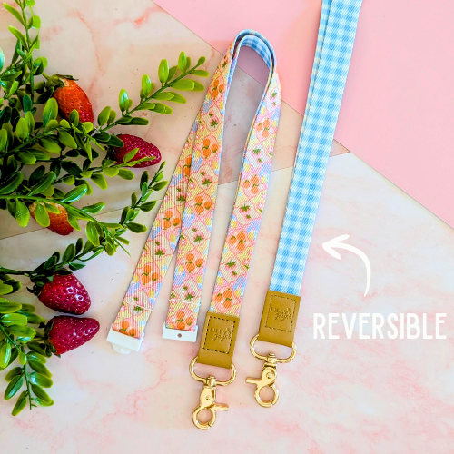Two reversible fabric straps on a pink and white background with strawberries and greenery.