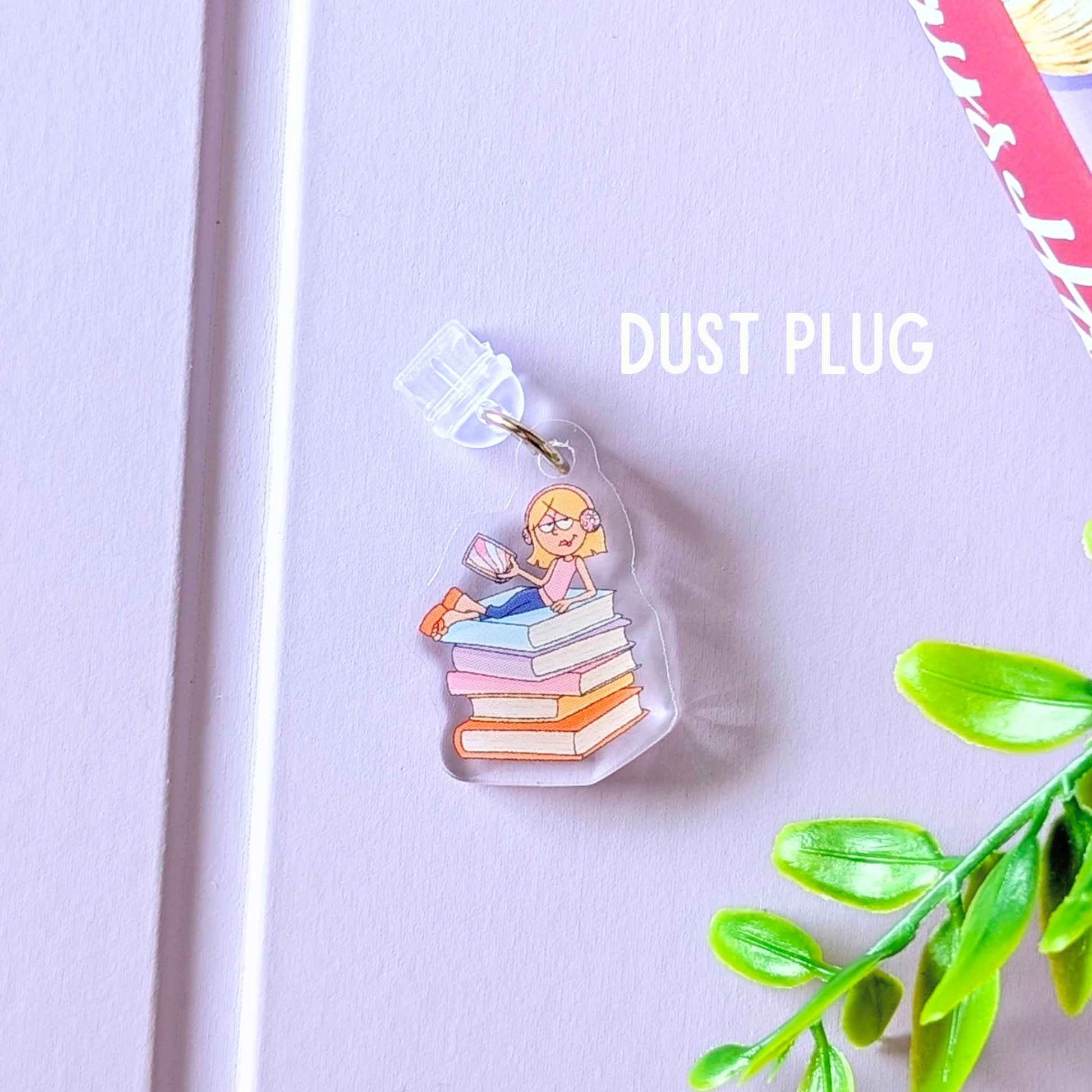 Dust plug with a design of a girl reading a book on books, on a light purple background with green leaves.