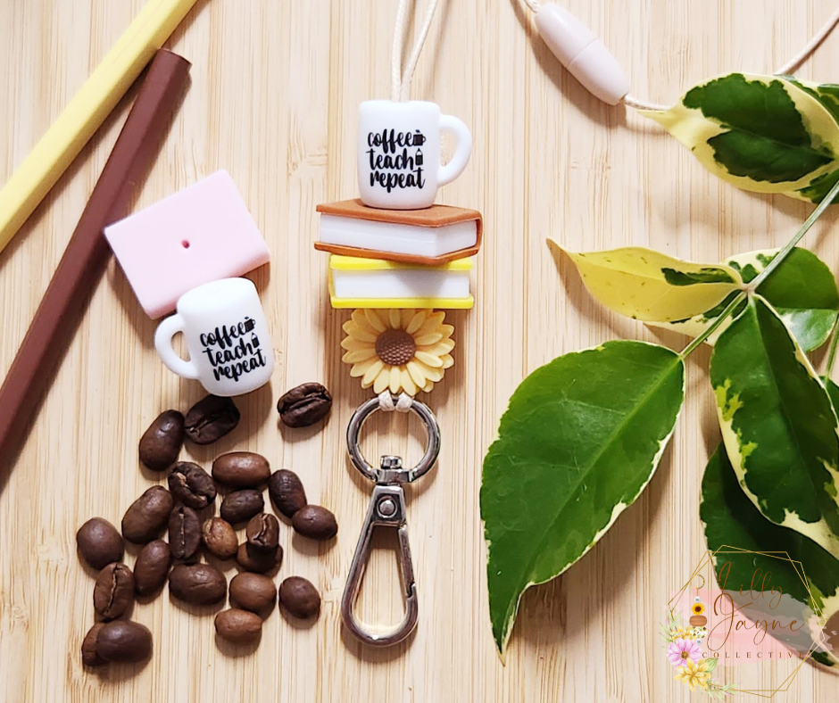 The Lilly Jayne Collective Coffee Teach Repeat Teacher Lanyard features a keychain with mini coffee mug charms, sunflowers, and stacked books—perfect for teachers who love coffee. The mugs read coffee teach repeat.
