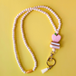 Beaded lanyard with a pink apple-shaped charm on a yellow background