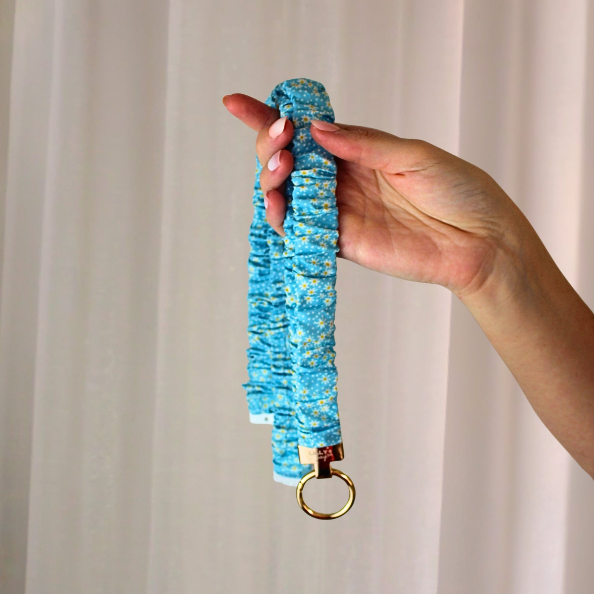 Hand holding a blue textured lanyard with a gold ring against a beige curtain background