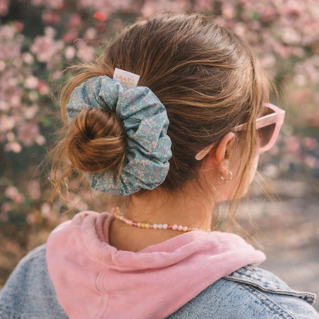 Person wearing a floral scrunchie in their hair with a blurred floral background
