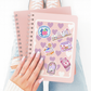 Pink notebook with stickers held by a hand, with a white background