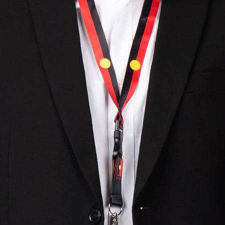 Person wearing a black suit with a white shirt and a red lanyard with yellow buttons.