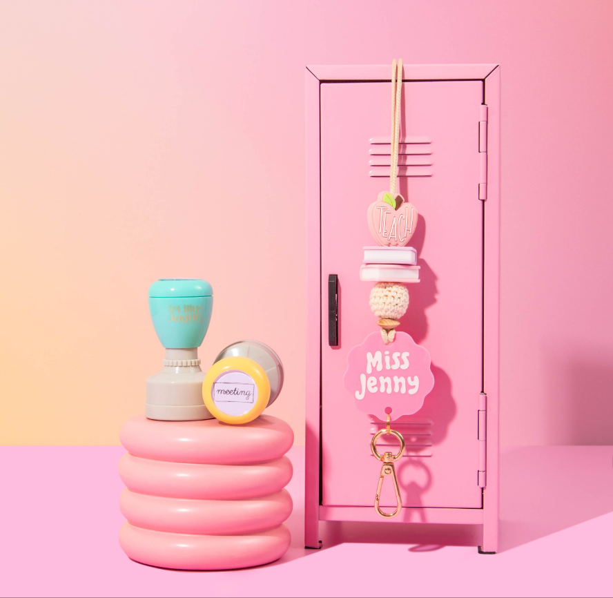 A pink personalized lanyard with a floral pattern and the name 'Miss Jenny' printed on it, displayed on a pink mini locker. alongside a pair of round pink earrings and a blue and yellow whistle.