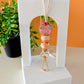 A lanyard featuring a multicolored floral silicone bead design with a gold-colored clasp, displayed against a white stand with a plant in the background.