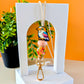 A colorful lanyard featuring a kookaburra design with silicone beads, displayed on a white stand with an orange background and a plant to the side.
