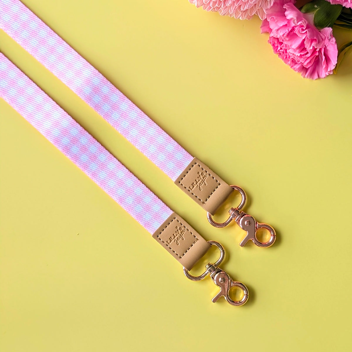 Pink and white checkered strap with beige leather buckle and gold hardware on a yellow background with pink flowers.