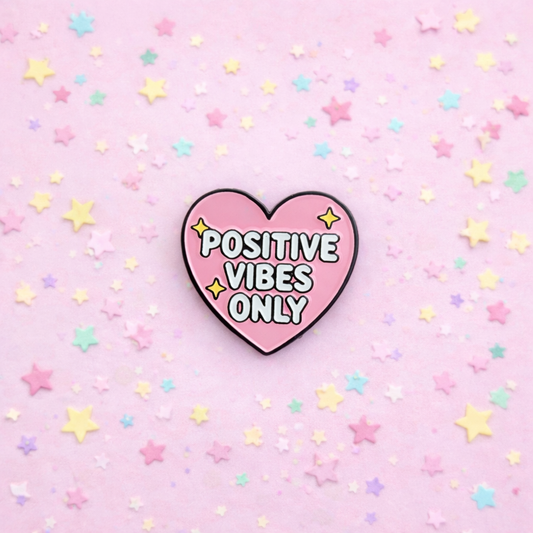 Heart-shaped 'Positive Vibes Only' pin on a pink background with stars