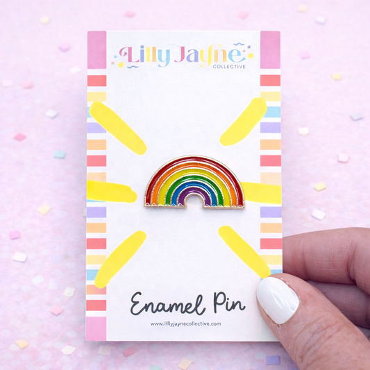 Rainbow enamel pin on a card with 'Lilly Jayne Collective' branding, held by a hand.
