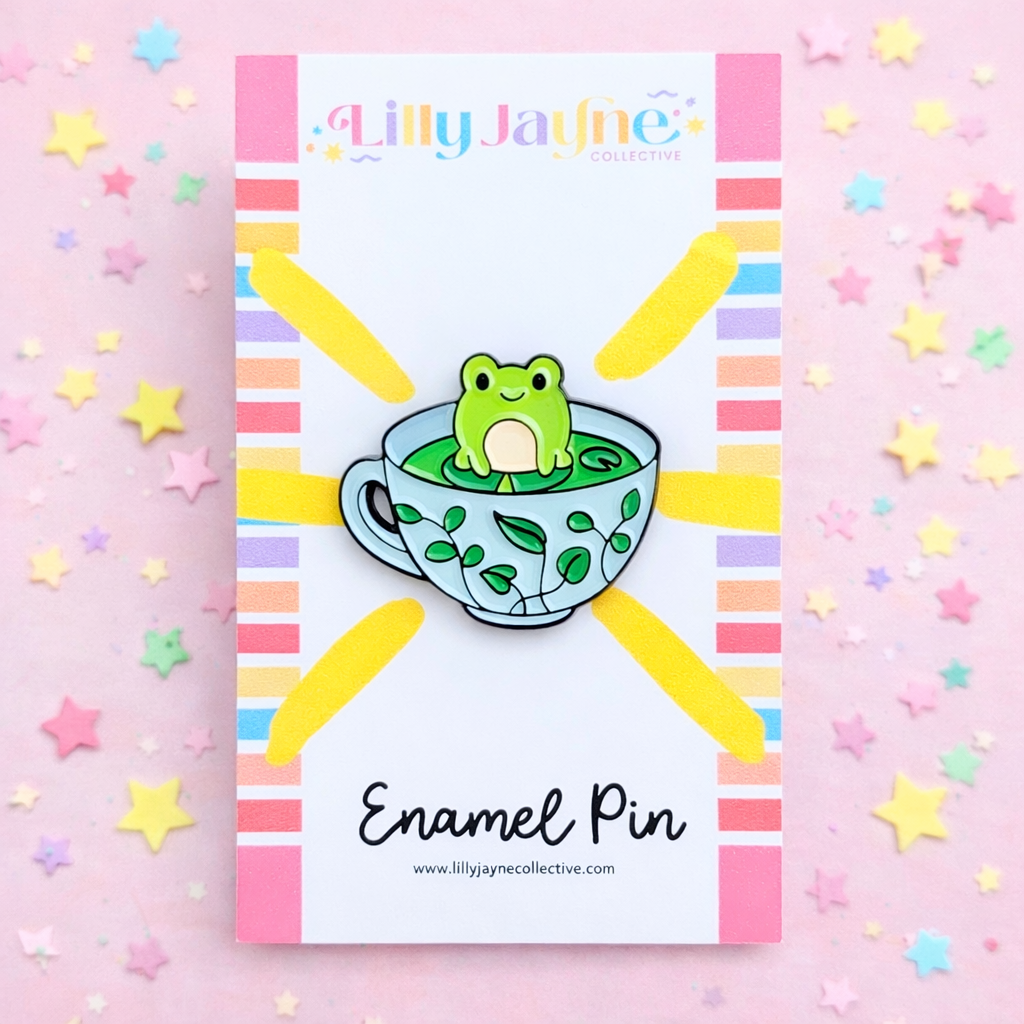 Enamel pin with a frog in a teacup design on a colorful background