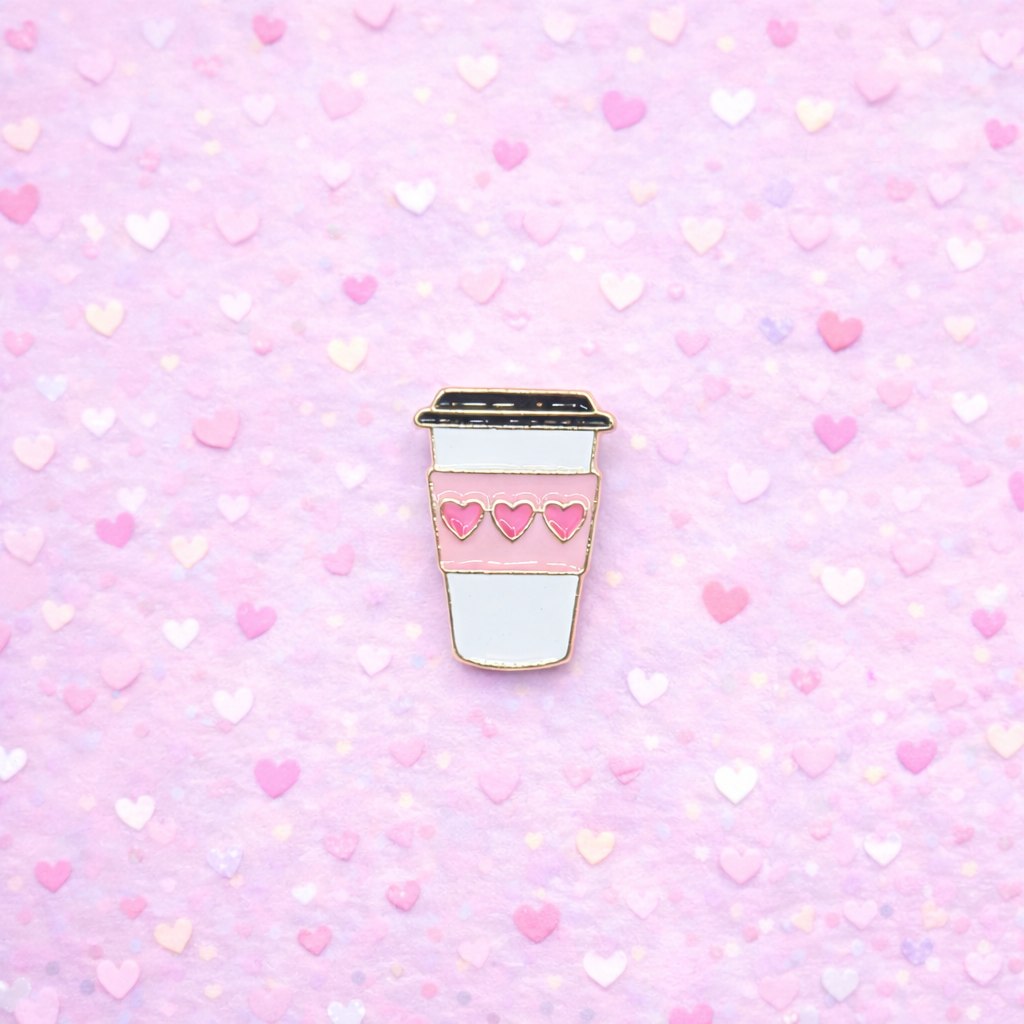 Enamel pin of a coffee cup with heart designs on a pink heart-patterned background