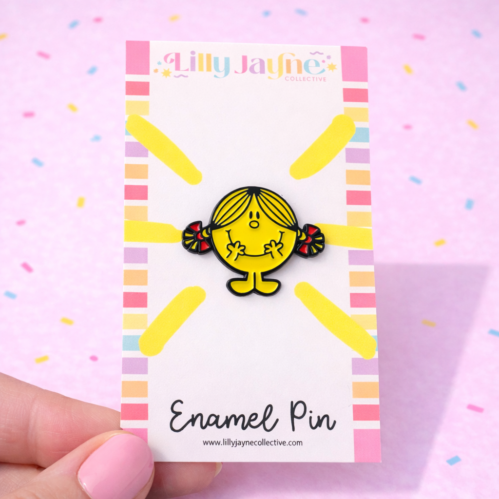 Enamel pin on a card with colorful border, held against a pink background.