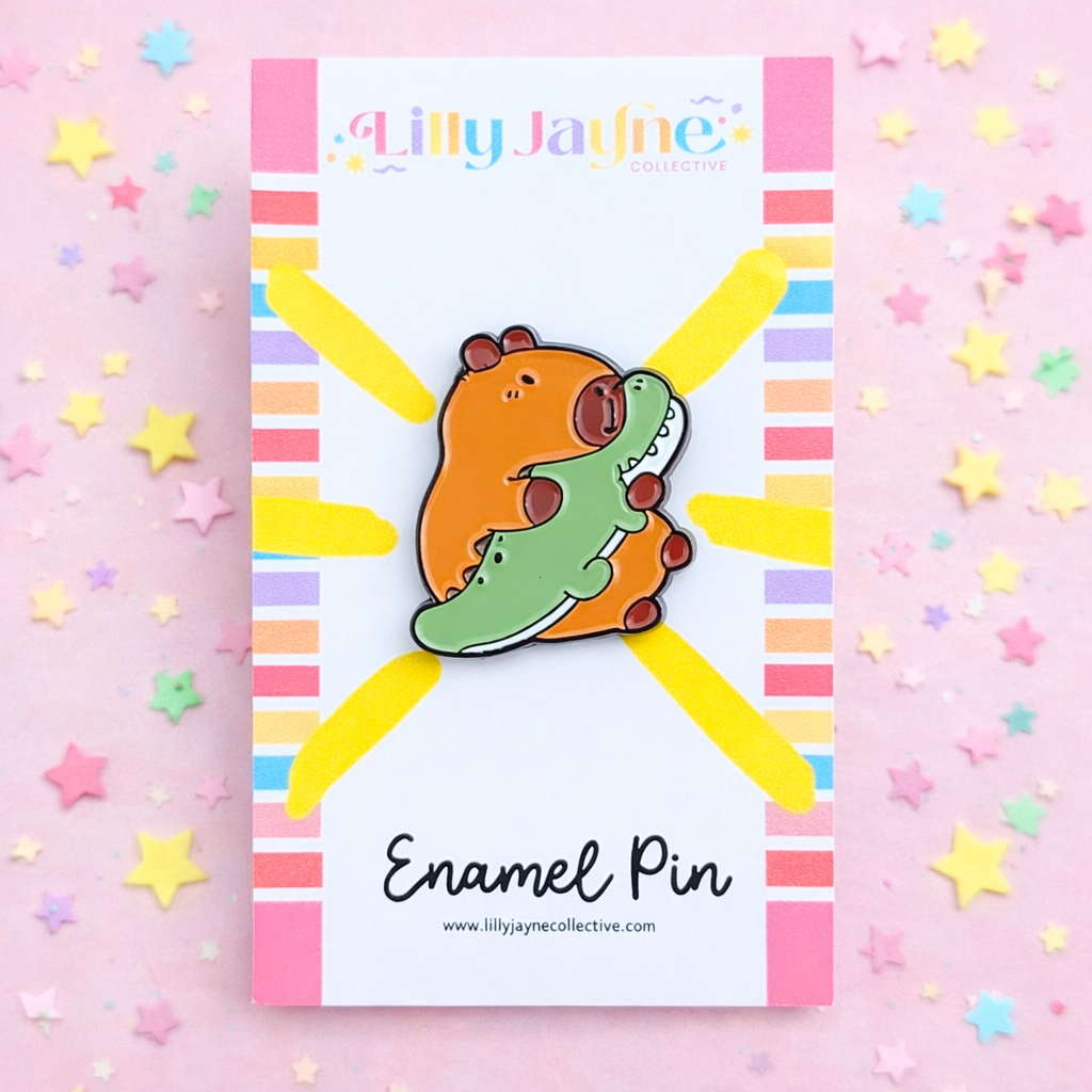Enamel pin on a colorful card with 'Lilly Jayne Collective' branding, surrounded by star-shaped confetti on a pink background.