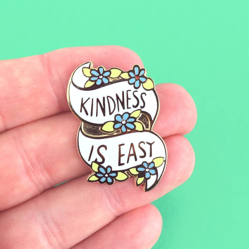 Pin with 'Kindness is Easy' text held between fingers against a green background
