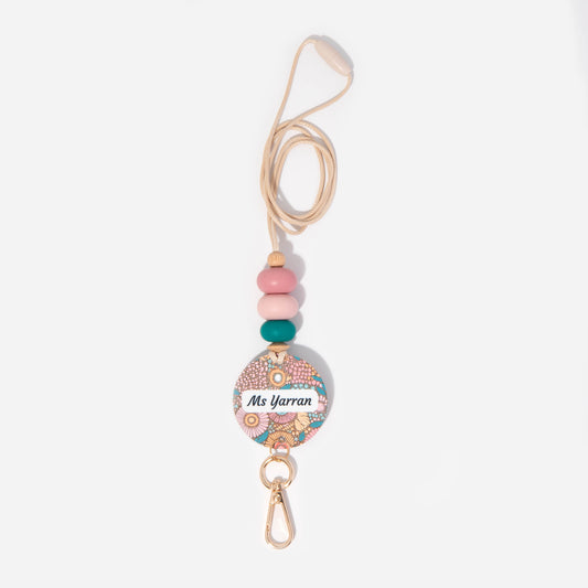 A personalized lanyard featuring a round name tag with floral patterns, attached to a metal clip and a key ring, with colorful silicone beads on the strap.