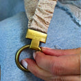 Load image into Gallery viewer, Gold belt buckle with 'Jayme' branding on a beige belt, held by a hand against a blue denim background.

