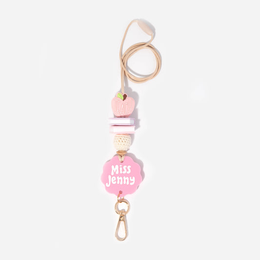 A pink personalized teacher lanyard with a name tag and floral pattern, featuring a gold-colored breakaway clasp and a metal clip.
