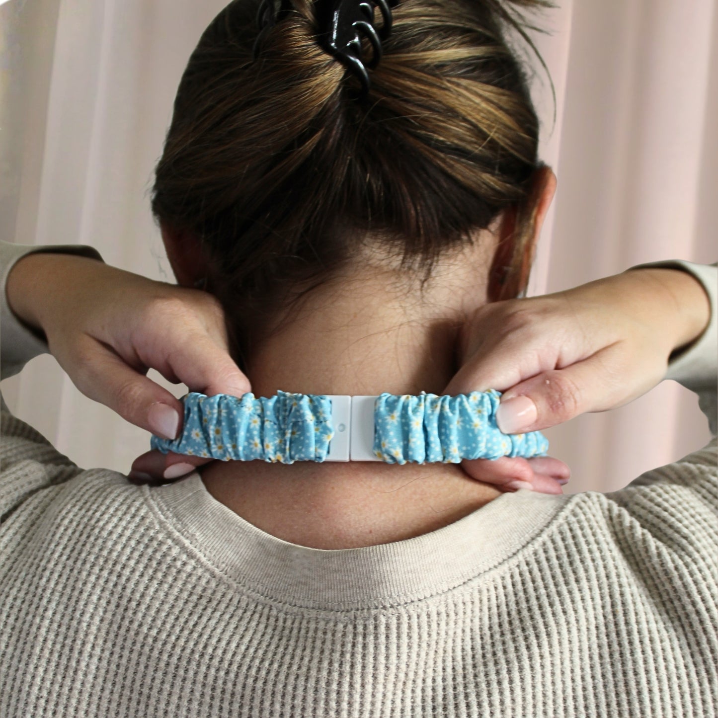 Person wearing a blue scrunchie on their wrist with a neutral background
