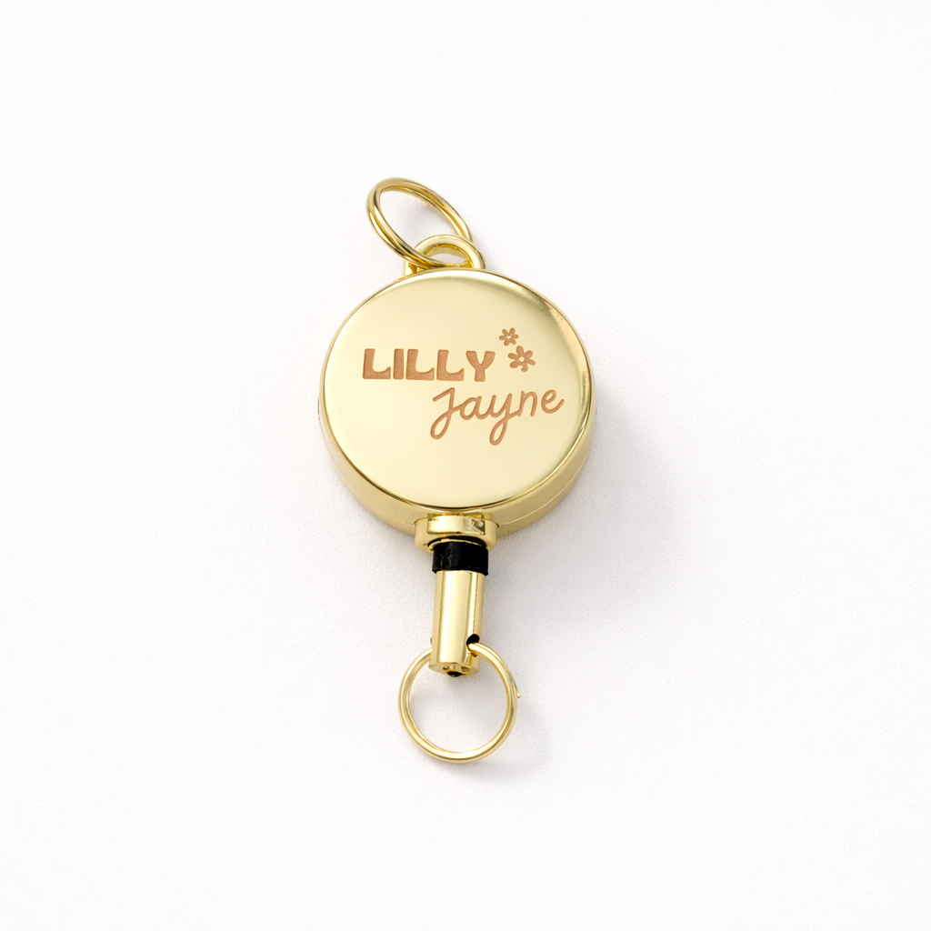 Gold retractable badge holder with 'LILLY JAYNE' engraving on a white background