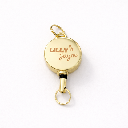 Gold retractable badge holder with 'LILLY JAYNE' engraving on a white background