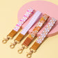 Four colorful keychains with patterned straps on a pink and yellow background