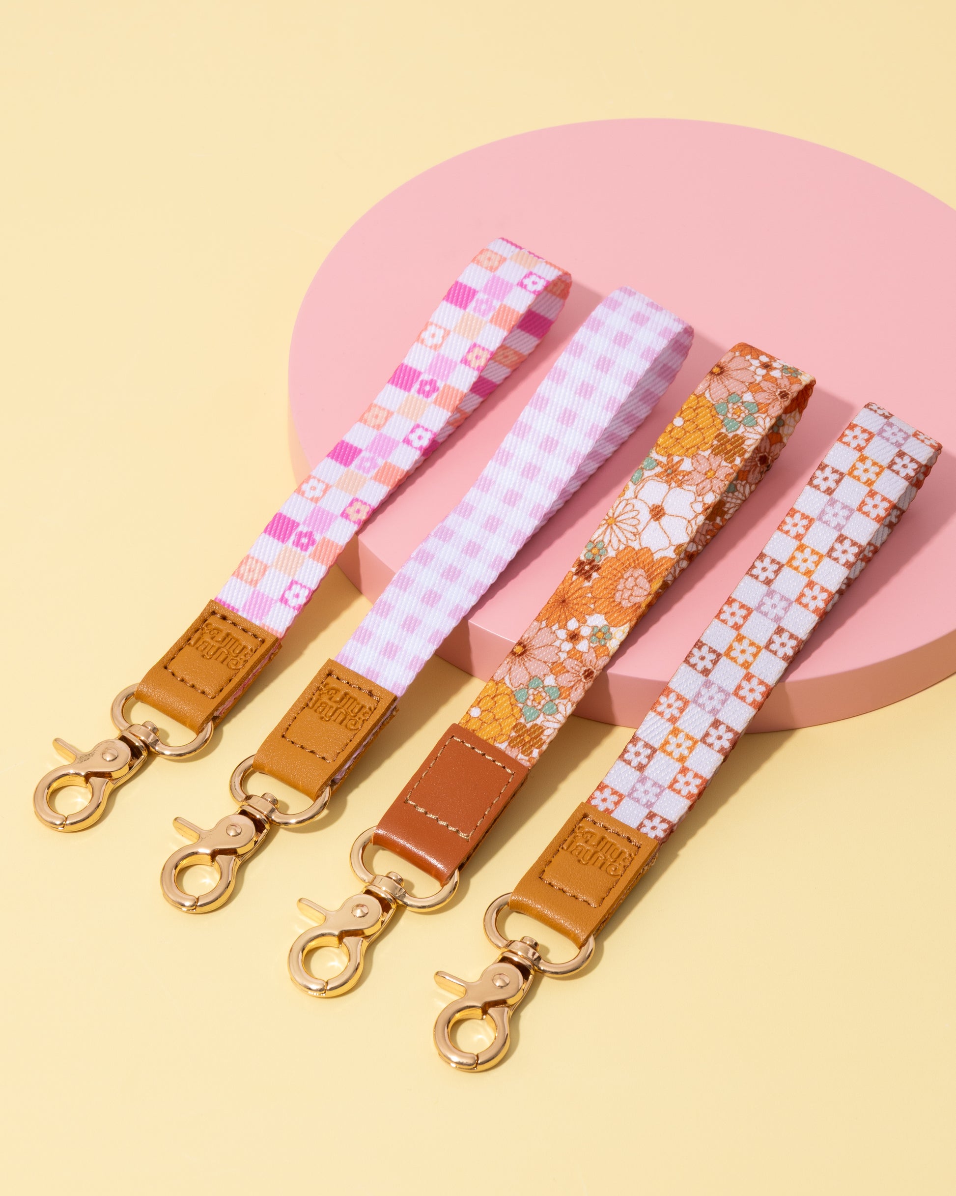 Four colorful keychains with patterned straps on a pink and yellow background