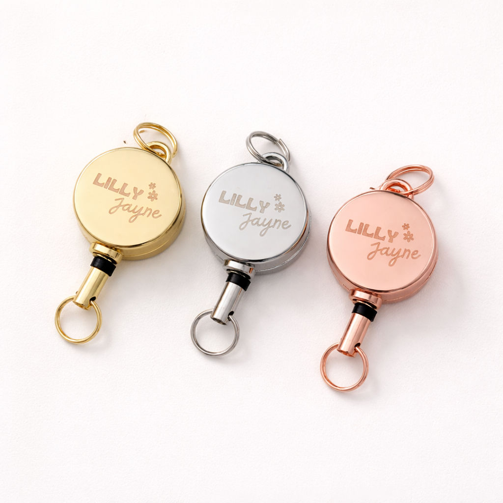 Three retractable keychains in gold, silver, and rose gold on a white background.