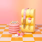 Colorful children's products including a yellow seat, pink inflatable cup holder, and keychains on a checkered floor with pink background.